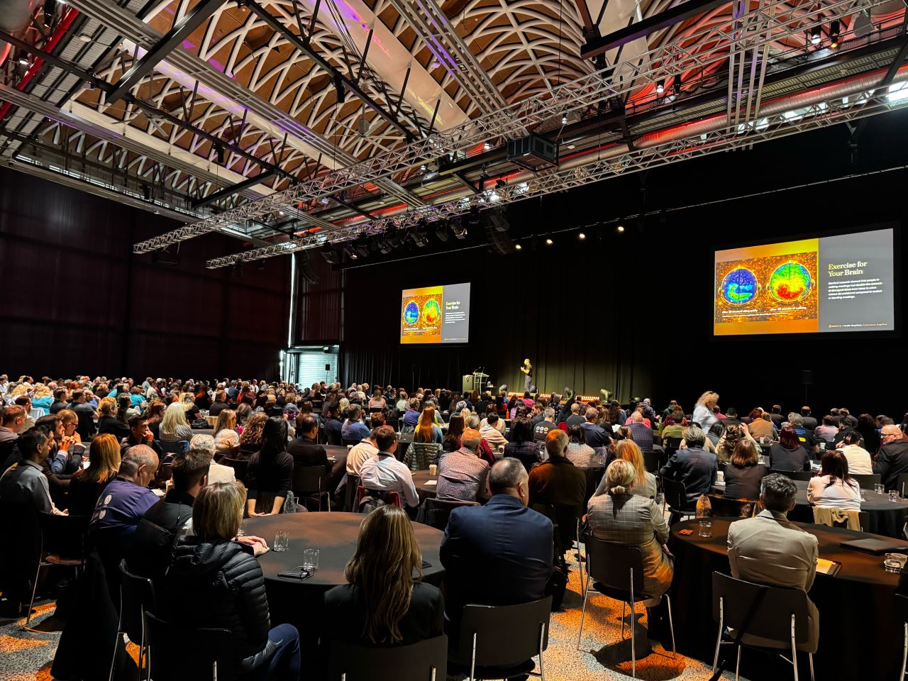 Olly on stage at AIM 2026, addressing a large conference audience
