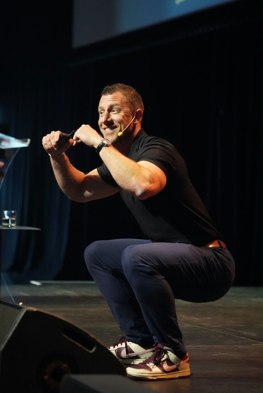 Olly Bridge smiling while demonstrating a squat on stage